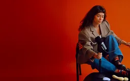 A woman seated against a red wall in a Dame campaign shot