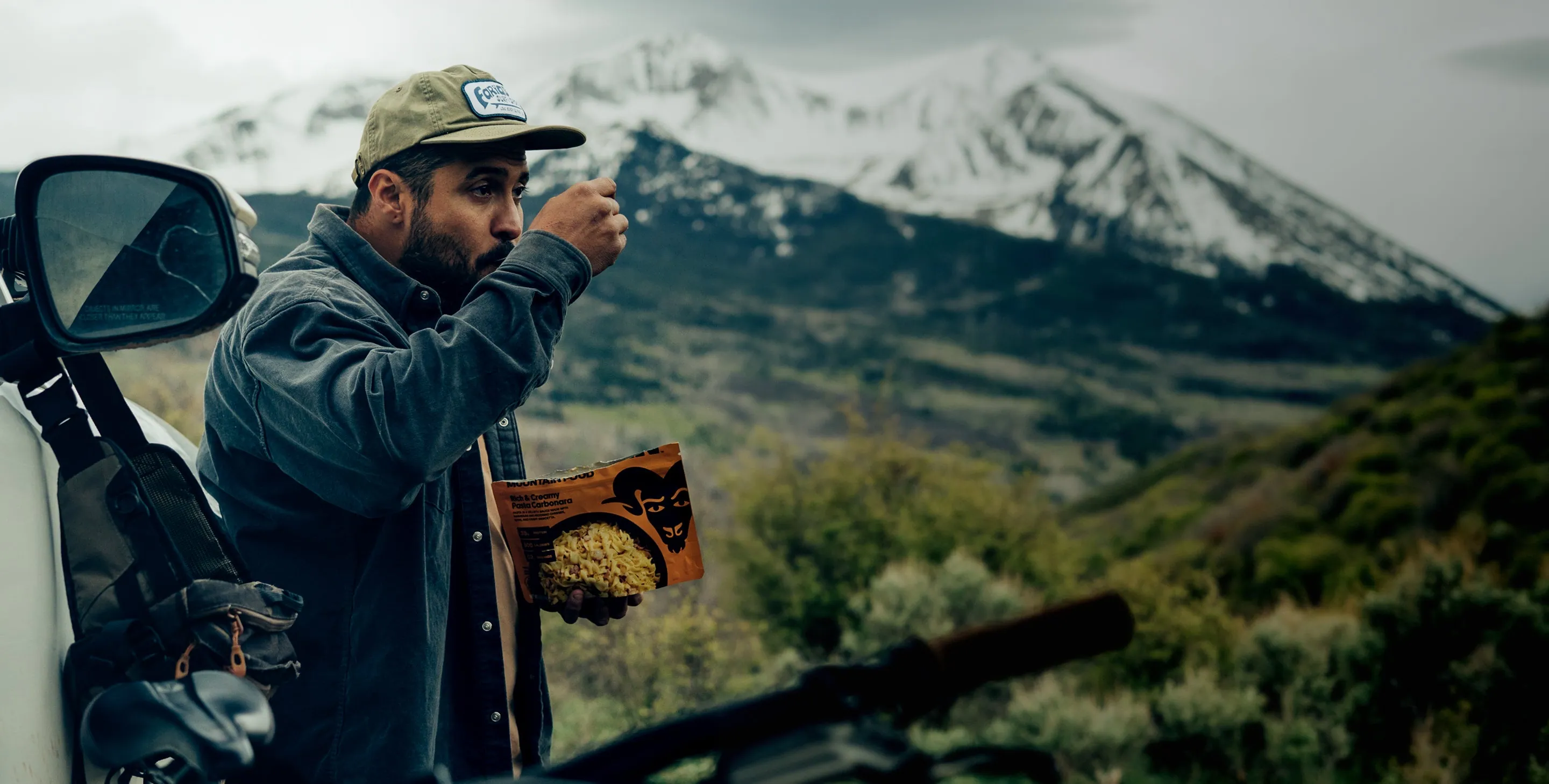 A camper eating a Bighorn meal beside a truck in the mountains