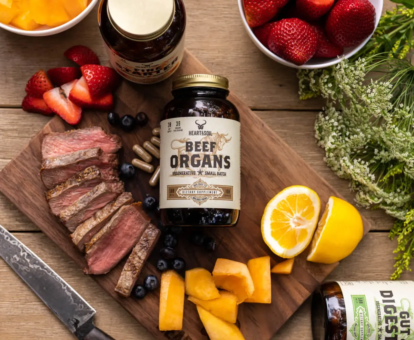 Sliced steak, a Beef Organs jar, lemon and wildflowers on a wooden board